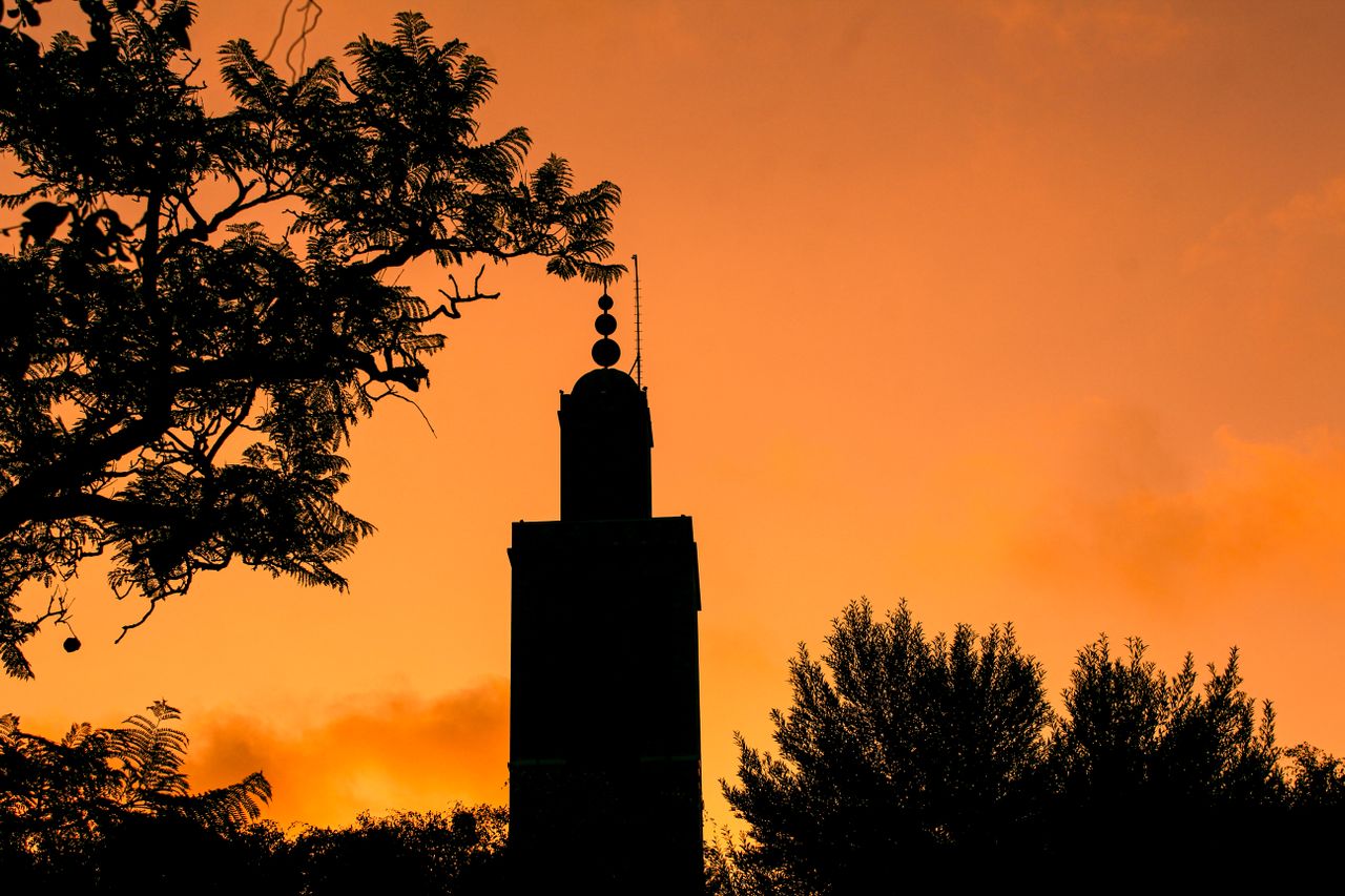 A minaret silhouetted against a glowing orange sky at sunset in Morocco